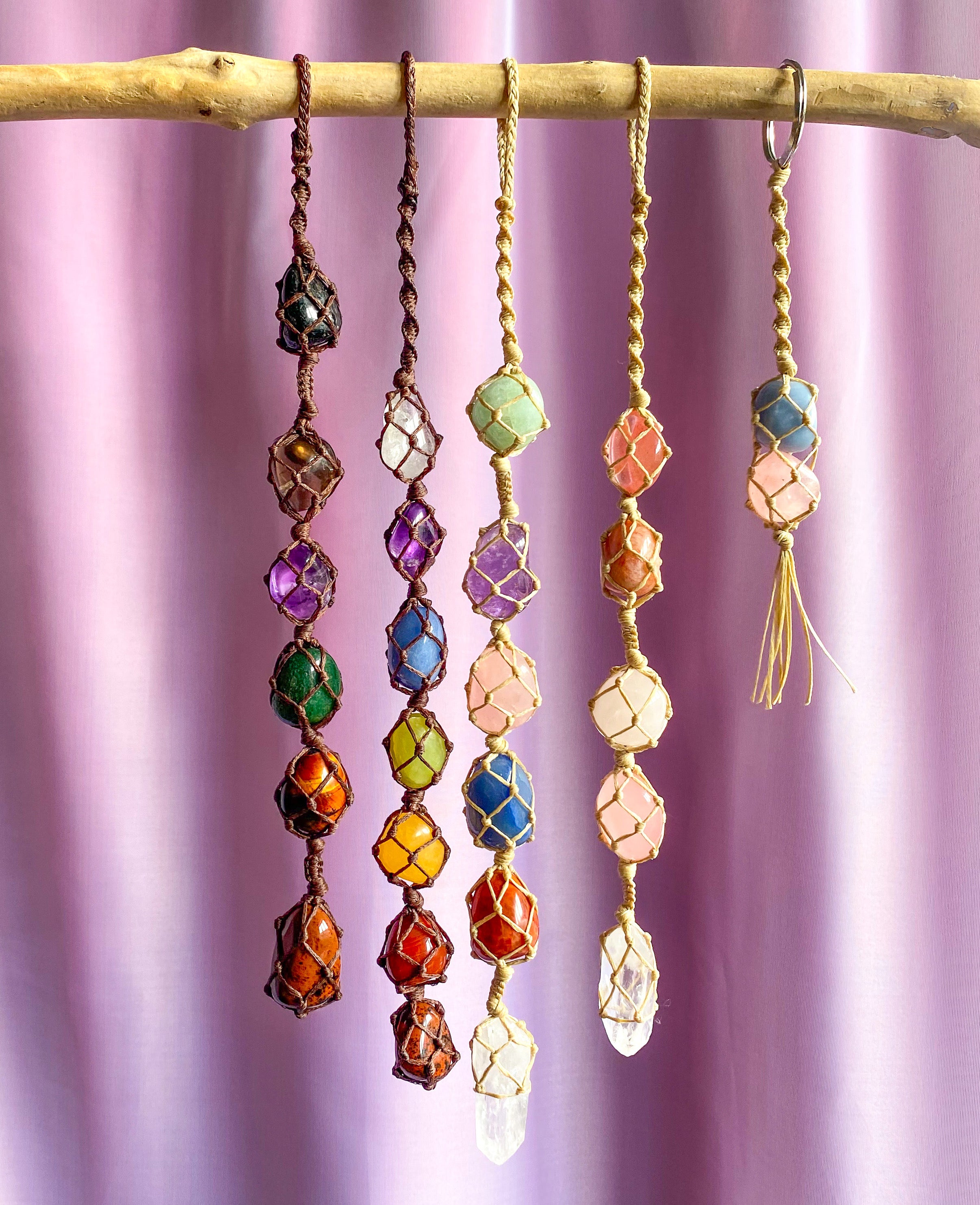 crystal macrame hangings on a wooden stick, against a pink backdrop 