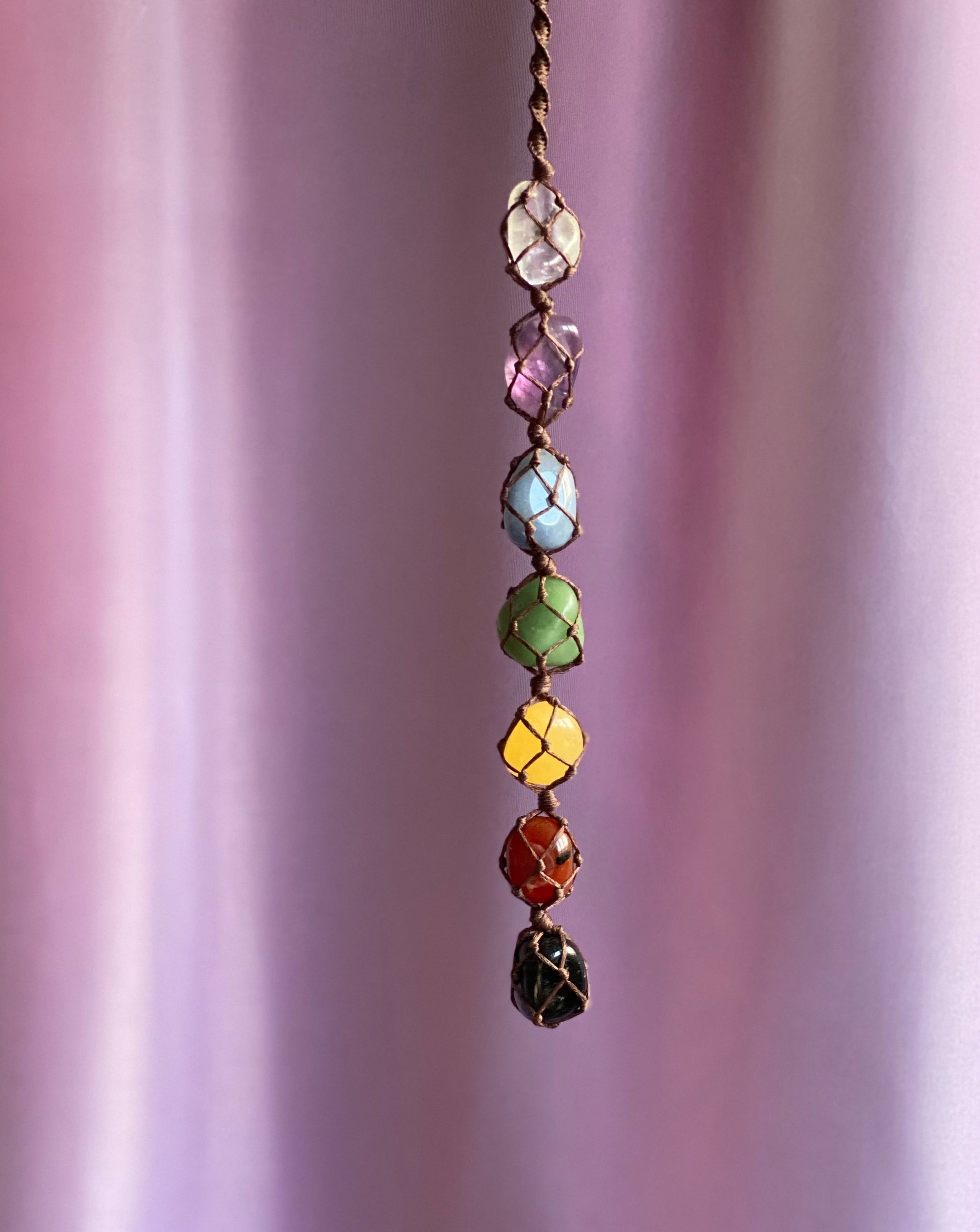 macrame wall hanging that drops vertically with chakra crystals - clear quartz, amethyst, blue quartz, green aventurine, yellow calcite, fire agate, black obsidian. wrapped in a brown cotton cord